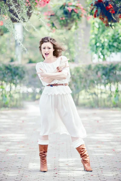 Portret van mooie glimlachend witte Kaukasische meisje vrouw met lang donker rood bruin haar, in witte zomerjurk, permanent in bloemen in de zomertuin van het park buiten, plezier — Stockfoto