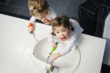 Closeup portrait of twins kids toddler boy girl in bathroom toilet washing face hands brushing teeth with toothbrash playing with water, lifestyle home style, everyday moments, top view clipart