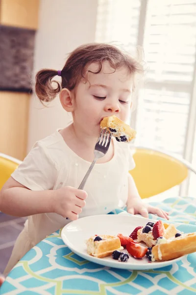 Potret satu bahagia putih Kaukasia anak gadis balita dengan ekor babi dalam gaun putih makan sarapan buah wafel dengan garpu di dapur dini hari — Stok Foto