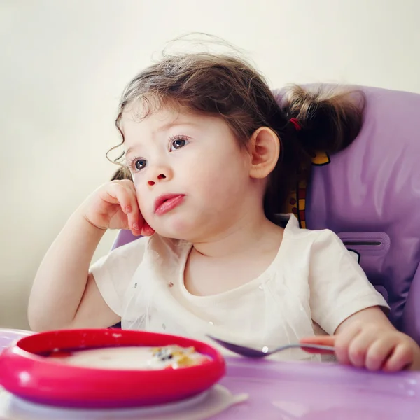 Potret gadis kecil Kaukasia yang bosan duduk di kursi tinggi makan sereal dengan sendok di pagi hari, momen terus terang gaya hidup sehari-hari, kencang dengan filter Instagram — Stok Foto