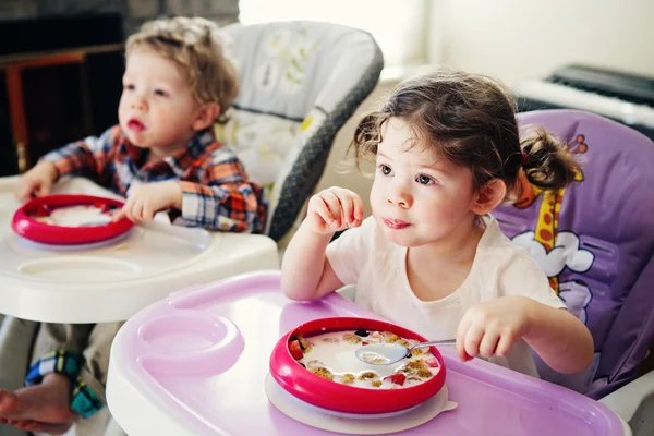 Portrait of cute adorable Caucasian children twins siblings sitting in high chair eating cereal early morning, everyday lifestyle candid moments, toned with Instagram filters — Stock Photo, Image