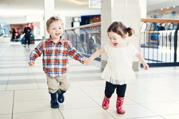 Portrait of two cute adorable babies children kids toddlers friends siblings running in mall store laughing smiling holding hands, going shopping — Stock Photo, Image