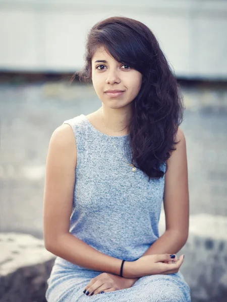 Porträt einer schönen lateinamerikanischen Frau mit braunen Augen, langen dunklen lockigen Haaren im grauen Kleid, die im Park sitzt und lacht und in die Kamera schaut, Lifestyle-Portraitkonzept — Stockfoto