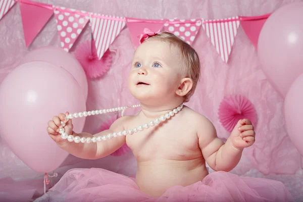 Portrait of cute adorable Caucasian baby girl with blue eyes in pink tutu skirt celebrate his first birthday with gourmet cake and balloons looking away, cake smash first year concept — Stok Foto