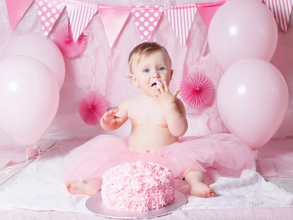 Retrato de bonito adorável menina caucasiana com olhos azuis em saia de tutu rosa comemorando seu primeiro aniversário com bolo gourmet e balões olhando na câmera, conceito de primeiro ano bolo smash — Fotografia de Stock