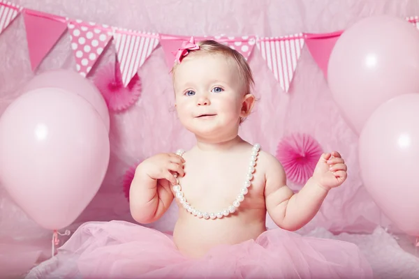 Portrait of cute adorable Caucasian baby girl with blue eyes in pink tutu skirt and pearls celebrated his first birthday with balloons looking in camera, cake smash first year concept — Stok Foto