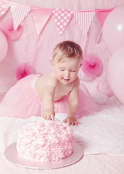 Portrait of cute adorable Caucasian baby girl with blue eyes in pink tutu skirt celebrate his first birthday with gourmet cake and balloons looking away, cake smash first year concept — Stok Foto