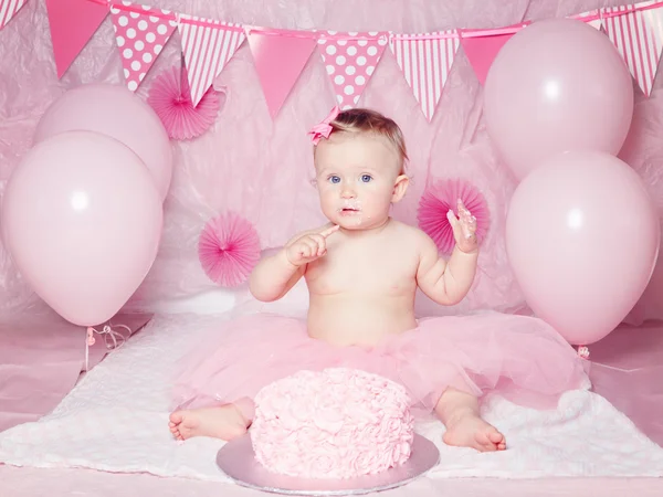 Portrait of cute adorable Caucasian baby girl with blue eyes in pink tutu skirt celebrate his first birthday with gourmet cake and balloons looking in camera, cake smash first year concept — Stok Foto