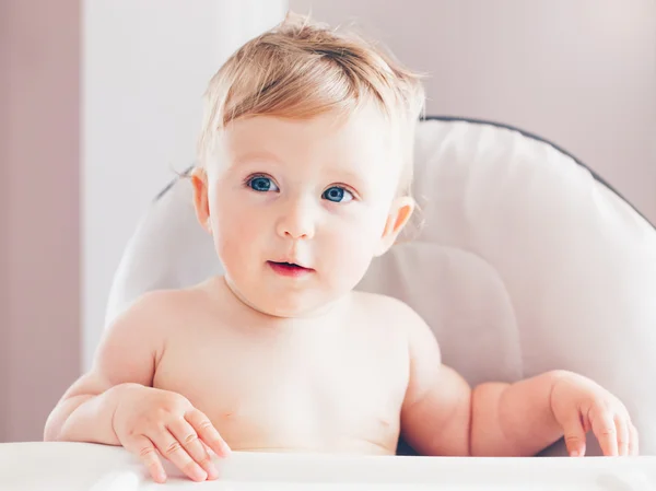 Closeup portrait of cute adorable funny blonde Caucasian smiling laughing baby boy girl with blue eyes with emotional face expression sitting in high chair in kitchen looking away — Stock Photo, Image