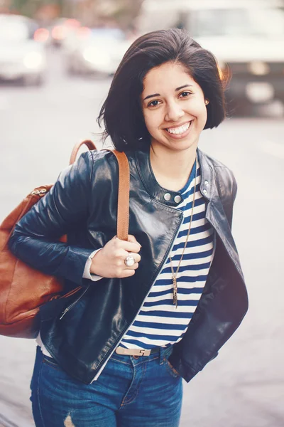Retrato de una hermosa joven muchacha latina caucásica sonriente con ojos marrones oscuros, pelo corto y oscuro, en jeans azules, chaqueta motorista de cuero con mochila en el exterior de la ciudad, tonificada con filtros Instagram —  Fotos de Stock