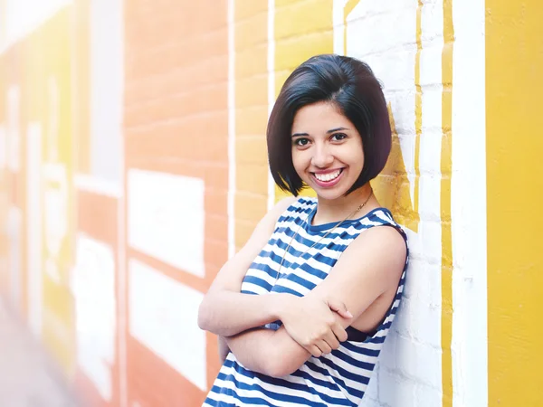 Retrato de bela sorridente jovem hipster latino hispânico menina mulher com cabelo curto bob, em azul branco tshirt listrada, inclinando-se na parede de tijolo na cidade olhando para a câmera, estilo de vida conceito de moda — Fotografia de Stock