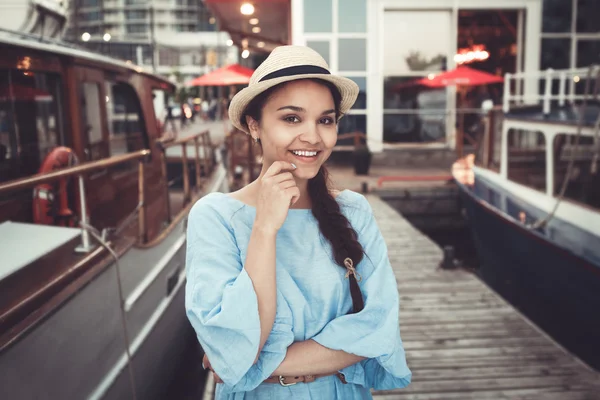 Портрет красивой улыбающейся белой брюнетки на причале яхтенного пирса, в синем платье и соломенной шляпе, концепция ретро-винтажного стиля морского флота — стоковое фото