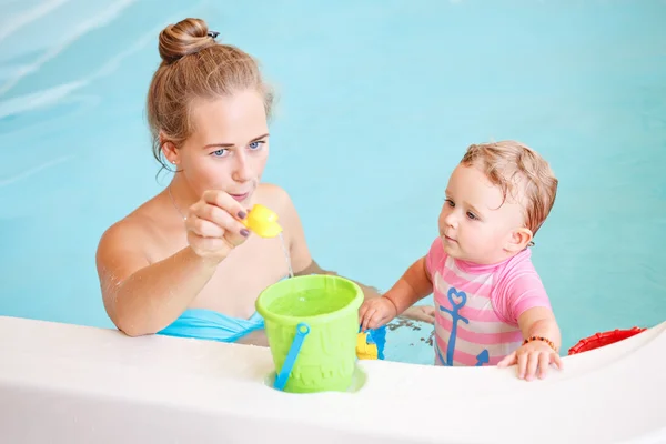 Group portrait of white Caucasian mother and baby daughter playing with toys in water on swimming poo nosing inside, training to swim, healthy active lifestyle — Stock Photo, Image