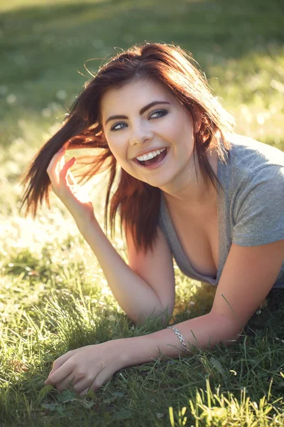 Closeup portret van mooie lachende jonge Kaukasische vrouw met rode zwarte haren, liggen op gras buitenshuis, lachen weergegeven: tanden, natuurlijke schoonheid jeugd kijken — Stockfoto