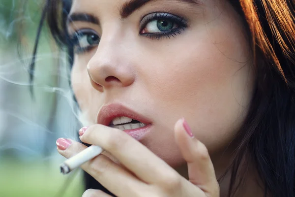 Primer plano retrato de blanco caucásico hermosa joven sexy morena mujer con luz azul ojos verdes fumar cigarrillo mirando en cámara, tonificado con filtros de Instagram, mal hábito malsano — Foto de Stock