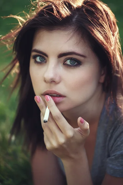 Closeup portrait of white Caucasian beautiful young brunette woman lying on ground grass smoking cigarette, toned with Instagram filters, bad unhealthy habit, lifestyle concept