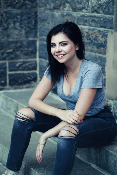 Portret van witte Kaukasische mooie jonge brunette meisje tiener met blauw groene ogen in geripte jeans, t-shirt, Keds glimlachend kijken in de camera. Afgezwakt met filters, lifestyle concept. — Stockfoto