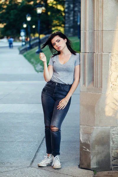 Retrato de branco caucasiano bela jovem morena adolescente em jeans e camiseta fora na cidade urbana no pôr do sol fumar cigarro olhando na câmera, tonificado com filtros Instagram — Fotografia de Stock