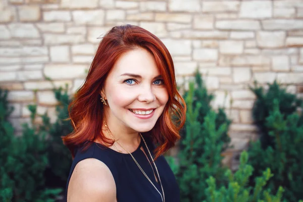 Retrato de close-up de mulher branca branca de meia idade sorridente com cabelo encaracolado ondulado vermelho em vestido preto olhando na câmera fora no jardim do parque, conceito de estilo de vida de moda de beleza — Fotografia de Stock