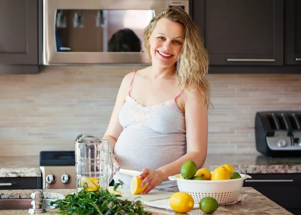 Porträt einer lächelnden weißen kaukasischen Blondine, die Zitruslimonade schneidet und Saft macht, zu Hause in der Küche steht und in die Kamera schaut, gesundes Lebensstilkonzept — Stockfoto