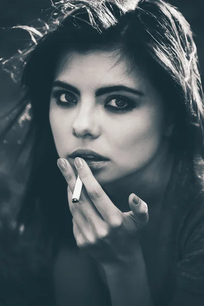 Closeup black and white portrait of white Caucasian beautiful young woman lying on ground grass smoking cigarette, bad unhealthy habit, lifestyle concept