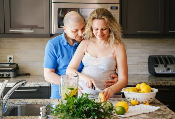 Portrait of smiling white Caucasian couple two people pregnant woman with husband cooking food fruit lemon juice, standing in kitchen, lifestyle healthy pregnancy happy life concept