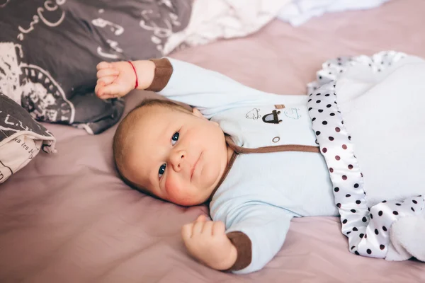 Retrato de bonito engraçado branco branco branco loiro menino recém-nascido com olhos azuis cinza deitado na cama dos pais grandes olhando na câmera, estilo de vida sincero, vida real — Fotografia de Stock