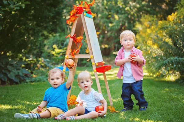 Grupo de três crianças brancas caucasianas crianças meninos e menina fora no verão parque de outono, desenhando cavalete segurando maçãs, jogando estudar aprendizagem, de volta à escola — Fotografia de Stock