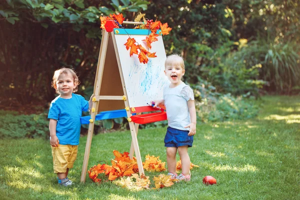 Grupo de dos niños blancos caucásicos niños niños y niñas de pie afuera en el parque de otoño de verano dibujando caballete con marcadores, jugando a estudiar el aprendizaje, de vuelta a la escuela —  Fotos de Stock
