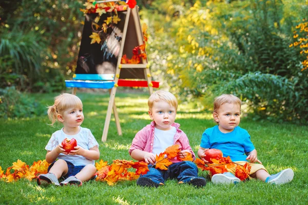 Grupo de três crianças brancas caucasianas crianças meninos e meninas sentados fora no parque de outono de verão, desenhando cavalete com folhas de outono e maçã, de volta à escola — Fotografia de Stock