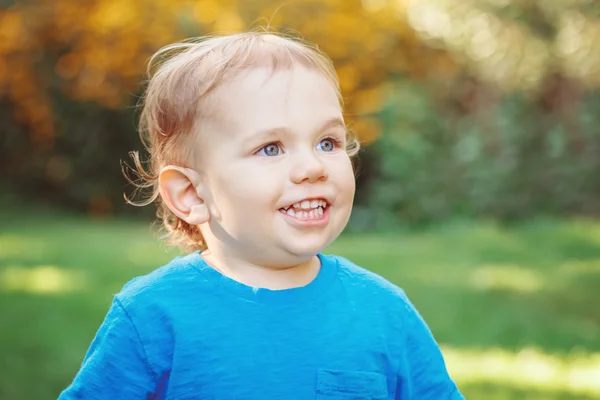 Retrato de bonito adorável rindo sorrindo branco caucasiano bebê menino criança de pé entre flores amarelas fora no jardim parque olhando para longe, estilo de vida conceito de infância feliz — Fotografia de Stock