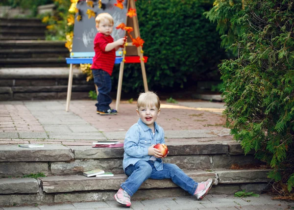 Groupe de deux enfants tout-petits blancs caucasiens garçons et filles dehors dans le parc d'automne d'été en dessinant un chevalet avec des marqueurs, des pommes, des livres, en jouant à étudier, en retournant à l'école — Photo