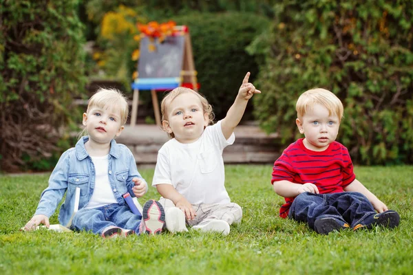 Grupp av tre vita kaukasiska småbarn barn kids pojkar och flicka sitter utanför i sommar höst park genom att rita staffli med hösten lämnar tittar i kameran, tillbaka till skolan — Stockfoto