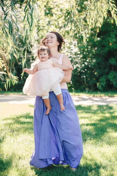 ライフ スタイル グループ白人ブルネット母持株ハグの娘は、公園で日当たりの良い夏の日に赤ちゃん子供と踊るピンクのドレスに白い笑顔の肖像画 — ストック写真