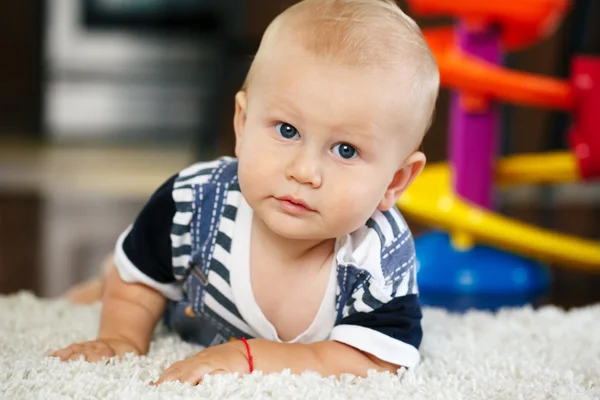 Portret van leuke schattige blonde Kaukasische lachende babyjongen met blauwe ogen liegen op verdieping in kinderen kinderkamer in de camera kijken — Stockfoto