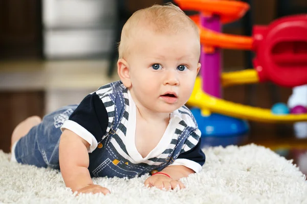 Portret van leuke schattige blonde Kaukasische lachende babyjongen met blauwe ogen liegen op verdieping in kinderen kinderkamer in de camera kijken — Stockfoto