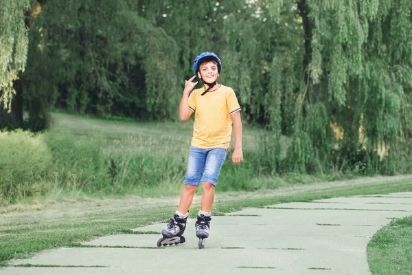 夏の日に公園の路上でヘルメット乗馬ローラースケートで幸せな笑顔白人の十代の少年 季節の屋外子供アクティビティスポーツ 健康的な子供時代の生活 — ストック写真