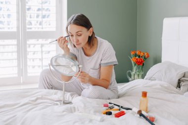 Orta yaşlı beyaz bir kadın sabah makyajını yapıyor. Genç bir kadın yatak odasında yatıp sabah rutinini yapıyor. Gerçekten özgün bir yaşam tarzı.. 