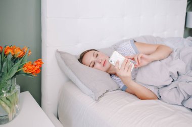 Güzel, orta yaşlı bir kadın sabahın köründe internette akıllı telefon sörfü yapıyor. Sosyal medyada arkadaşlarıyla konuşan genç bir kadın. Dijital internet bağımlılığı. Sabah rutini.