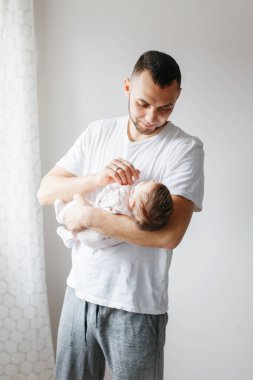 Genç, beyaz bir baba yeni doğmuş bir bebekle oynuyor. Sallanan bir çocuğun oğlunu elinde tutan bir ebeveyn. Otantik yaşam tarzı samimi anı. Aile hayatı. Babalar Günü.