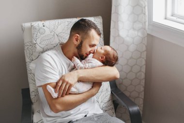 Babalar Günü tatili. Gururlu beyaz baba yeni doğmuş bebeği öpüyor. Anne ve baba, sallanan kız evlat oğlunu ellerinde tutuyor. Otantik yaşam tarzı samimi anı. Genç bekar baba aile hayatı.
