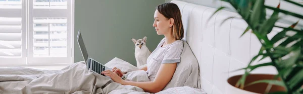 Middle age woman sitting in bed in morning with laptop surfing Internet. Young woman talking with friends in social media. Work from home. Digital online Internet addiction. Web banner header.