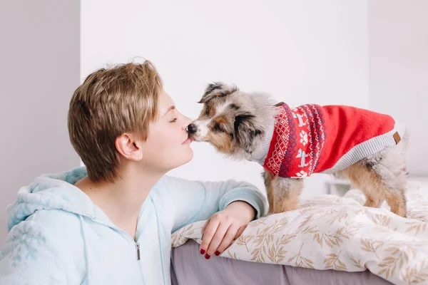 Young woman with short hair kissing cute puppy dog at home. Pet owner with little furry friend. Small pet dog licking its owner face. Relationship of domestic animal and human.