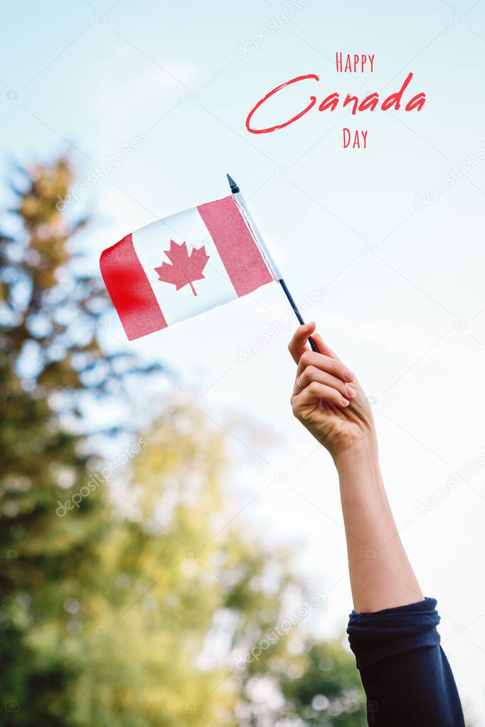 Happy Canada Day card with text. Closeup of woman human hand arm waving Canadian flag against blue sky. Proud citizen man celebrating national Canada Day on 1st of July outdoor. 