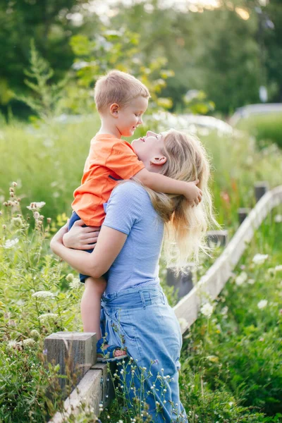 Mothers Day holiday. Young Caucasian mother and boy toddler son hugging embracing in park outdoor on summer day. Mom and child love and tenderness. Happy family childhood lifestyle.