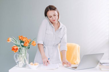 Masaüstü masasında dizüstü bilgisayarla çalışan orta yaşlı güzel bir kadın. Evden iş yapıyorum. Uzaktan eğitim ve çalışma. Cep telefonuyla konuşan genç bir kadın..