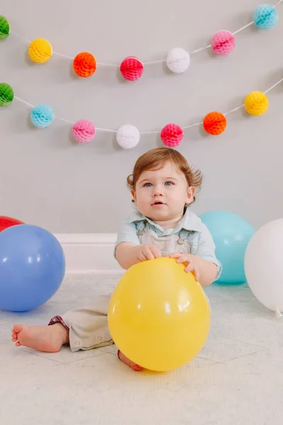 面白い白人の赤ん坊の男の子彼の最初の誕生日を祝う 子供の幼児はカラフルな風船で床に座っています 自宅でイベントやパーティーのお祝い 幸せな誕生日のライフスタイルのコンセプト — ストック写真