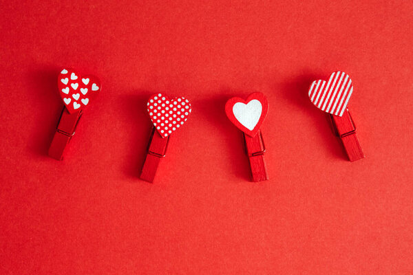 Valentine Day holiday. Four cute little small clothespins with pattern hearts on red crimson background with copyspace. Romantic dating love. Valentine day objects flat lay.