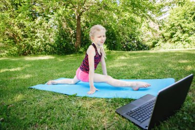 Beyaz bir kız çocuğu internette spor antrenmanı yapıyor. İnternette gerinen sanal yoga videoları. Çocuk evde dizüstü bilgisayarla antrenman yapıyor. Yeni normal. 