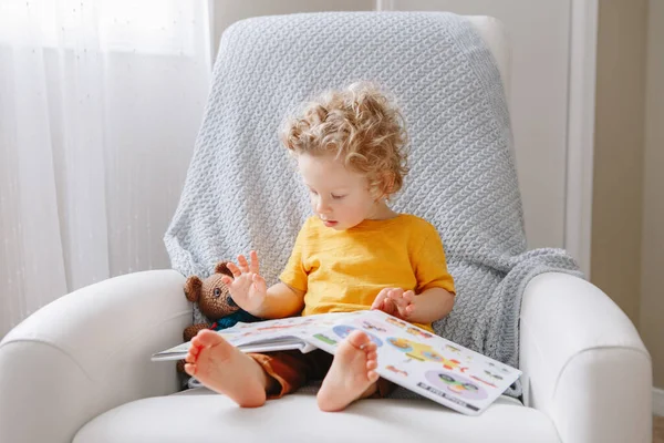 可爱可爱的小男孩蹒跚学步的2岁男孩坐在孩子房间的扶手椅上看书 幼儿发展教育 纯真的童年生活方式 — 图库照片